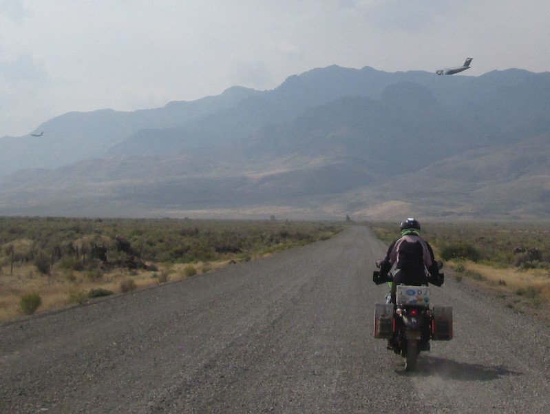 Jayne riding her
          motorcycle with military transport planes in the distance.