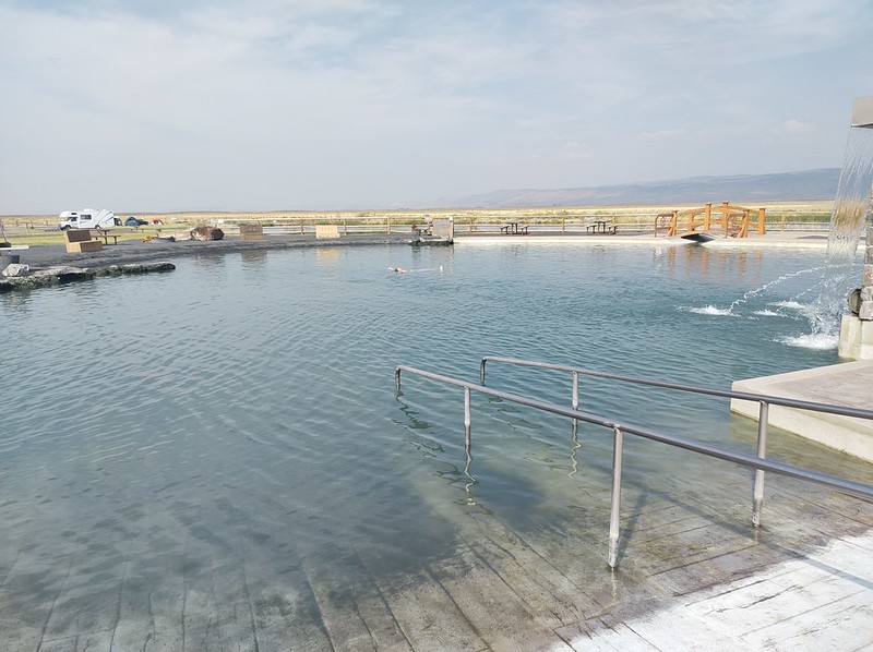 A large pool, surrounded by
          cement, with a desert landscape in the background. A tiny
          image of a woman is in the middle.