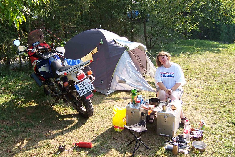 a woman sits at a pannier table and chairs at a motorcycle
        campsite